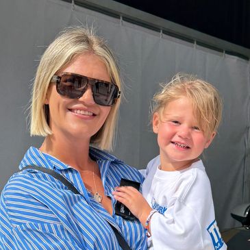 Woman and child smiling beside a racing car in a garage.
