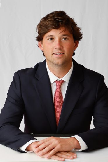 Young man in suit and red tie sitting with hands folded.