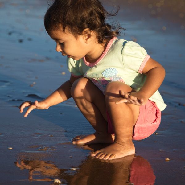 young girl, toddler playing on a beach with a reflection in the wet sand