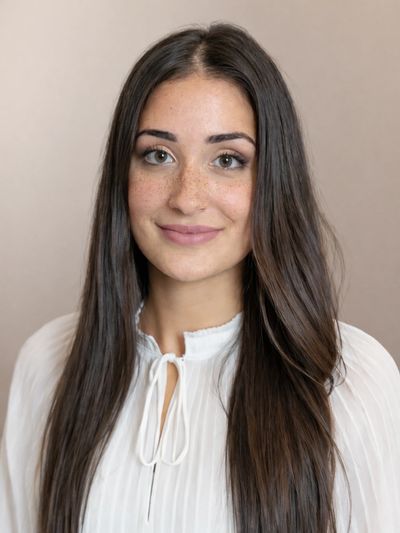 Porträt einer jungen Frau mit langen braunen Haaren und weißer Bluse.