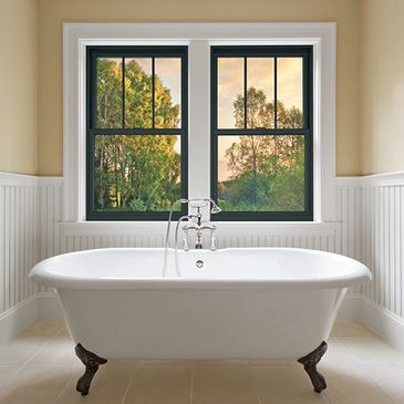Elegant clawfoot bathtub under a window with trees outside.