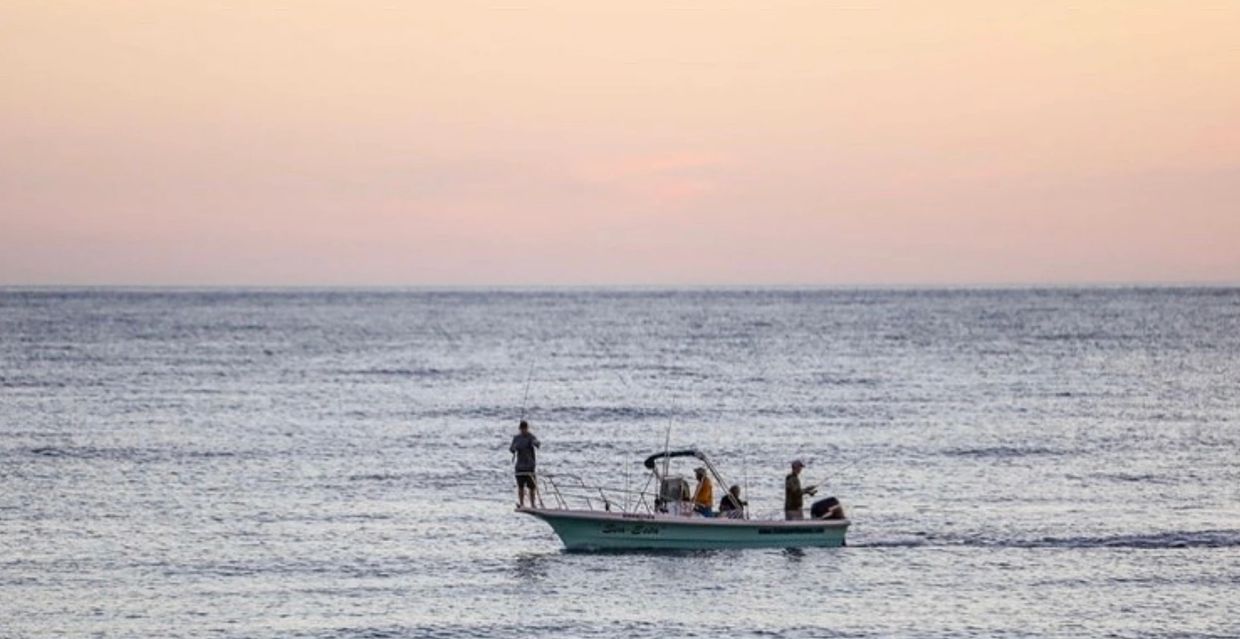 A small boat with three people fishing on calm waters at sunset.
