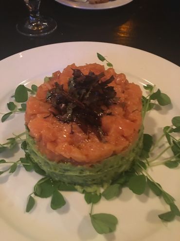 Salmon tartare with avocado and microgreens, beautifully plated on a white plate.