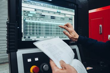 Person interacting with an industrial machine control panel while referencing a technical manual.