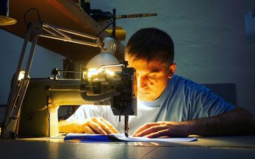 Man focused on sewing fabric with a sewing machine under bright light.