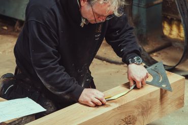 A man measuring and marking a wooden beam with tools.