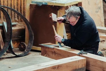 A craftsman chiseling wood with a mallet in a workshop.