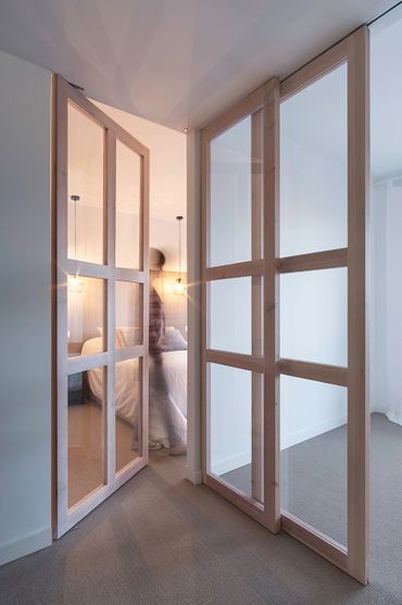 Wood-framed glass doors opening to a softly lit bedroom with a blurred figure.