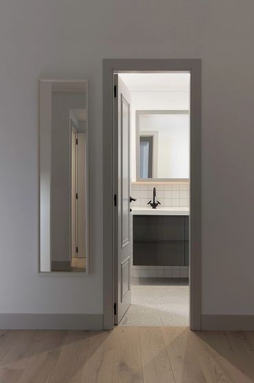 Minimalist bathroom entrance with a wall mirror and wooden flooring.