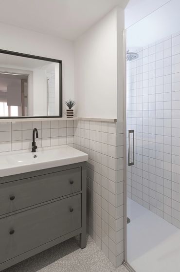 Minimalist bathroom with a gray vanity, black faucet, and glass shower door.