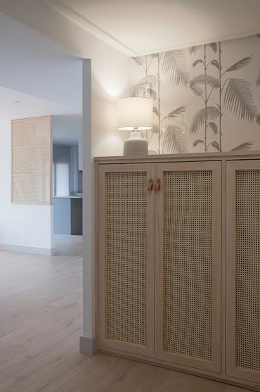 Cozy corner with rattan cabinet, soft lamp light, and botanical wallpaper.