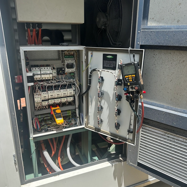Open electrical control panel with meters and wiring inside an industrial setup.