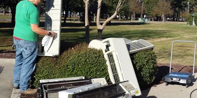 Man works outdoors on electronic equipment near a park.