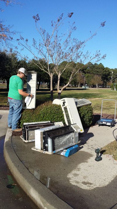Man cleaning and repairing multiple air conditioning units outdoors.