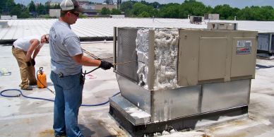 Man cleaning HVAC unit on rooftop with pressure washer.