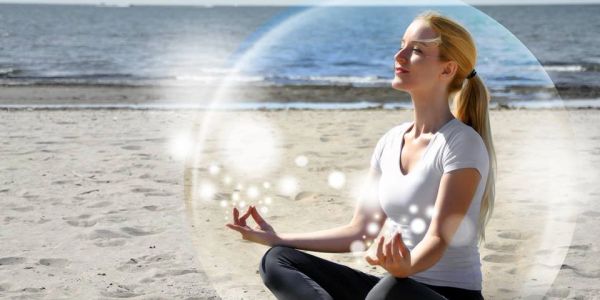 Woman meditating on the beach inside a glowing protective bubble.