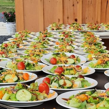 Rows of salad plates prepared for a large outdoor event.