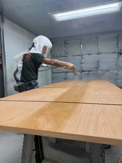 Person spray-painting a large wooden surface indoors.