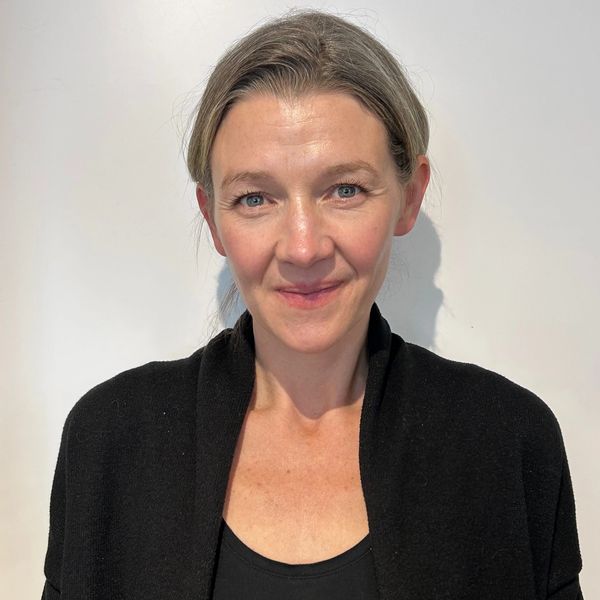 Smiling woman with light hair in a black top and cardigan against a white background.