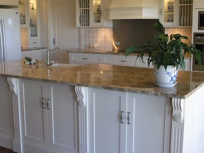Classic white kitchen with ornate island, marble benchtop, glass-front cabinets, and timber flooring.