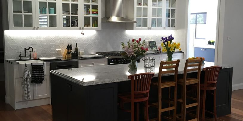 Traditional kitchen with white glass-front cabinets, dark island bench, marble top, and timber flooring in Maitland home.