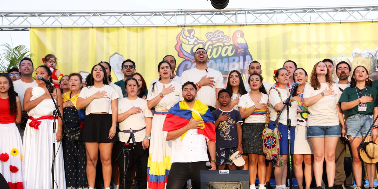 Group of people singing with hands on hearts, one wrapped in Colombian flag.