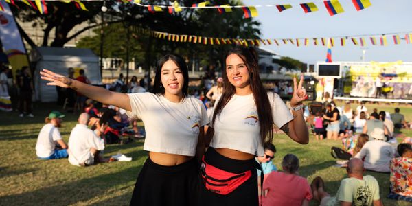Two young women smiling and posing at an outdoor festival with colorful flags.