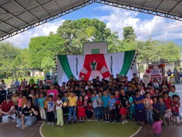 Gran grupo de niños y adultos en evento comunitario al aire libre.