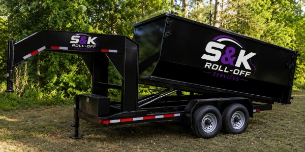 Black S&K Roll-Off Services trailer in grassy area.