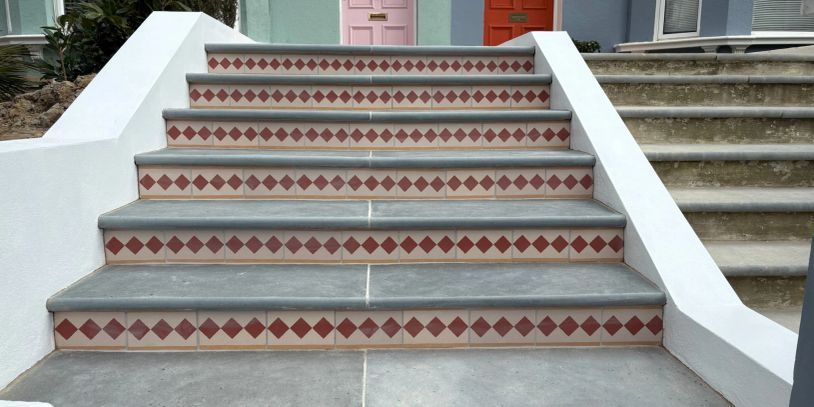 Stairs with red diamond tile pattern and colored doors in the background.