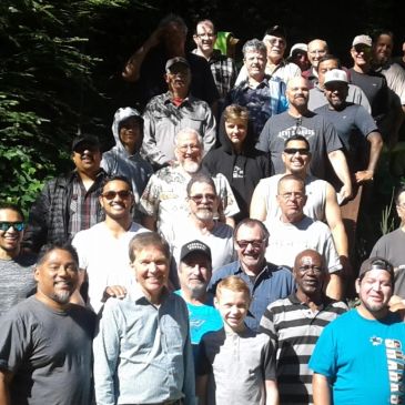 A large group of diverse adults posing outdoors in sunlight.
