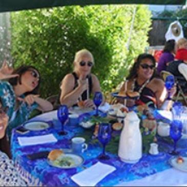 Group of women enjoying a meal outdoors at a table with blue glasses.