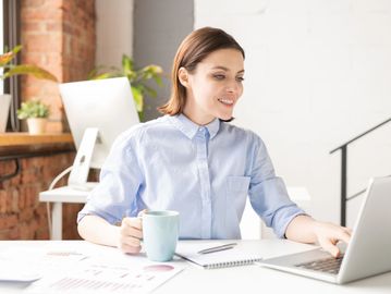 lächelnde Frau am Schreibtisch mit Tasse in der Hand im Coworking Space
