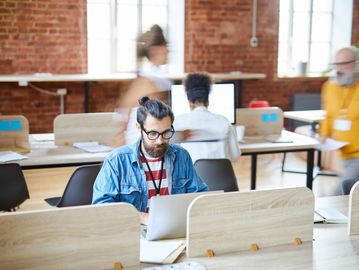 junger Mann mit Brille arbeitet am Laptop im Coworking Space