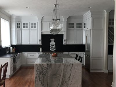 Modern white kitchen with marble island and black backsplash.
