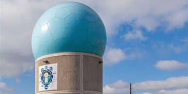 Large blue globe sculpture on a concrete pedestal against a cloudy sky.