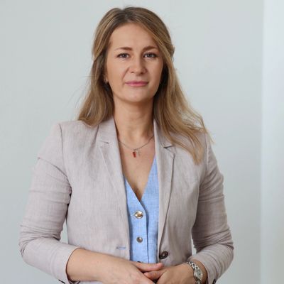 Frau in hellblauem Hemd und beigem Blazer, die selbstbewusst posiert.