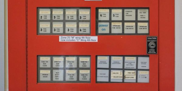 Fire alarm control panel with zone indicators and caution sign.