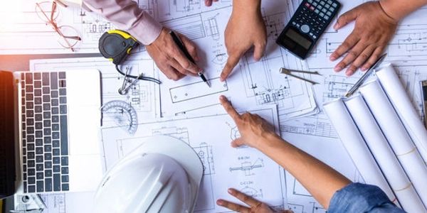 People discussing architectural blueprints with tools and laptop.
