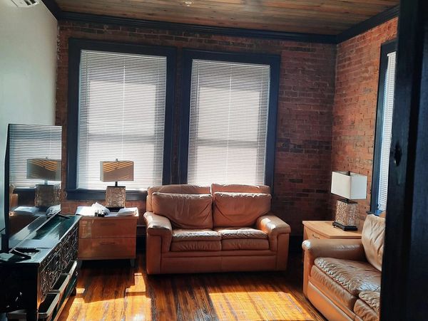 Cozy living room with leather couches, wooden floors, and brick walls.