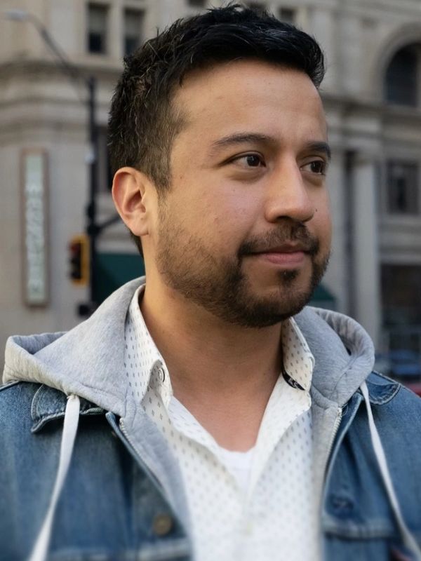 Young man with a trimmed beard in denim jacket and hoodie looking to the side.