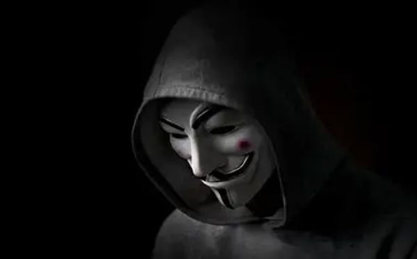 Person wearing a Guy Fawkes mask and a hood in dim light.