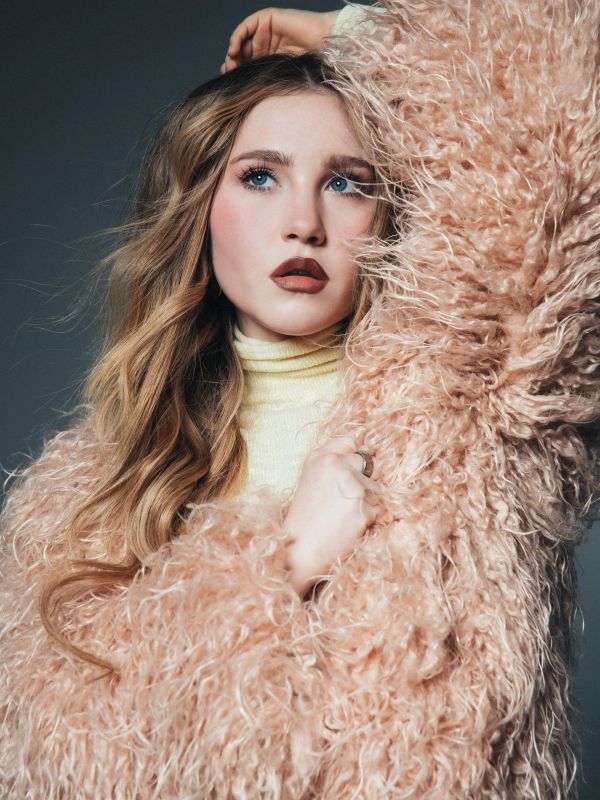Woman in fluffy peach jacket with curly hair.