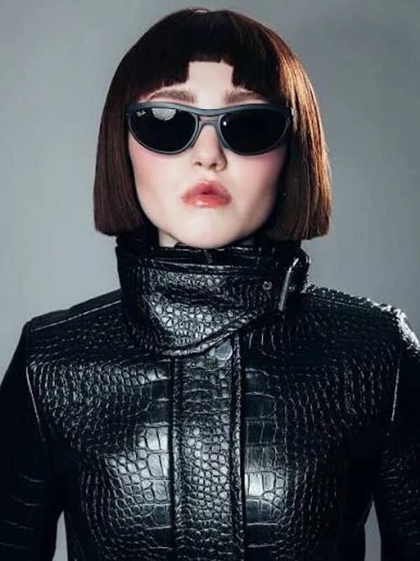 Woman with bob haircut, sunglasses, and black leather jacket.