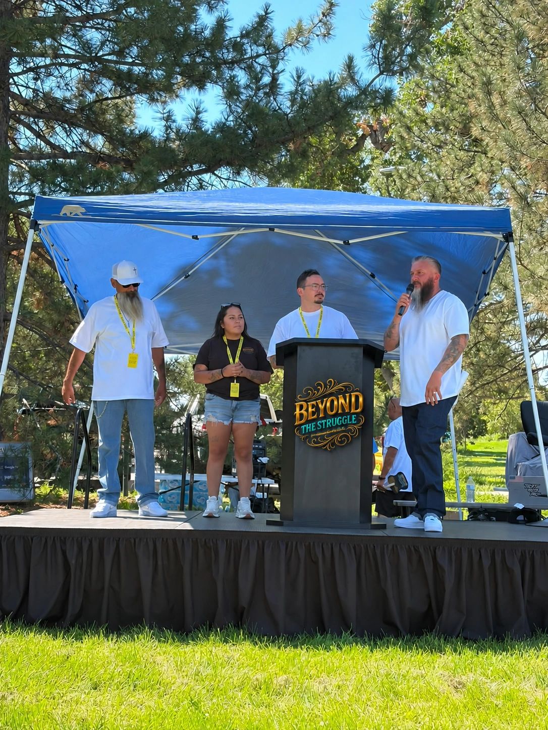 Four people speaking on an outdoor stage with a 'Beyond the Struggle' banner.