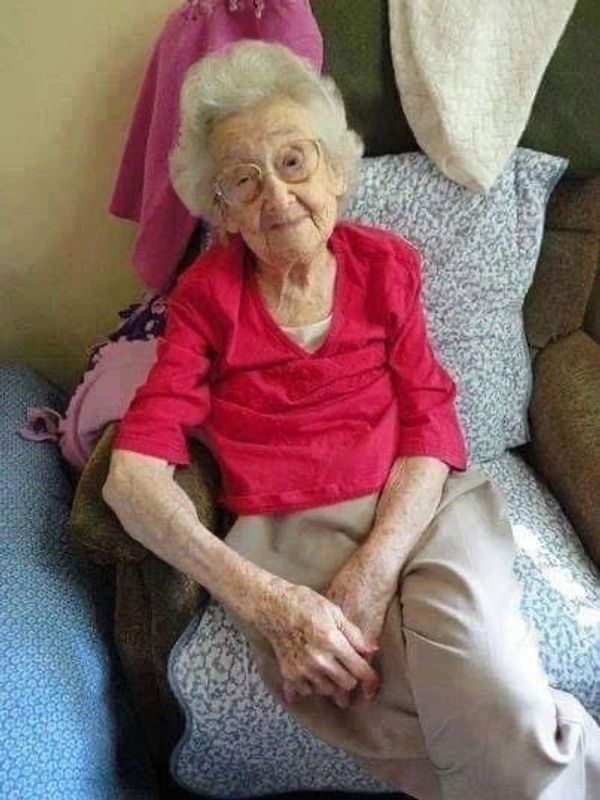 Elderly woman sitting on a couch, smiling gently.