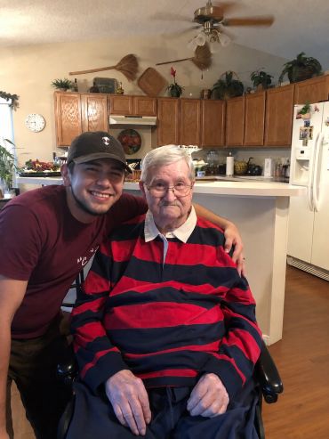 Young man smiling with an elderly man in a wheelchair.