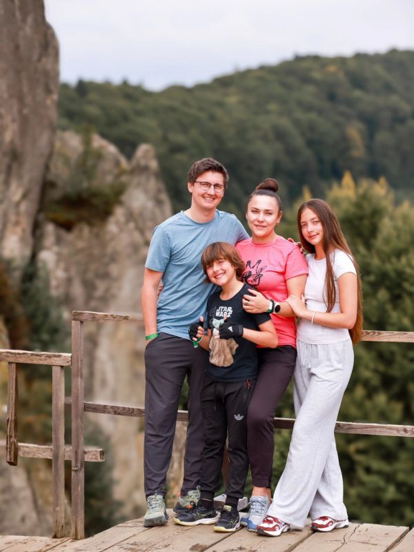 A happy family poses together outdoors with mountains in the background.