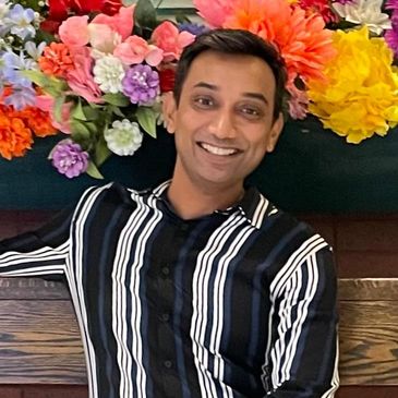 A smiling man in a striped shirt with colorful flowers in the background.
