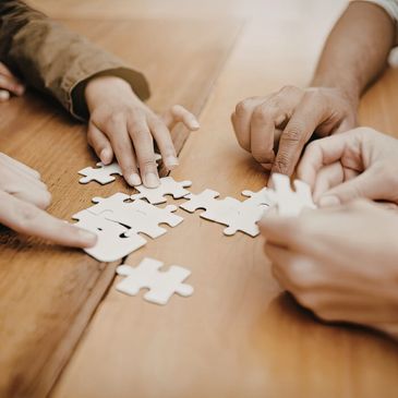 Hands working together to assemble a white puzzle on a wooden table.